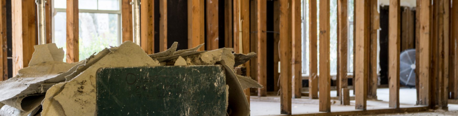 Intérieur en rénovation dont les murs ont été mis à nu, laissant voir l’ossature en bois, avec un tas de morceaux de plaques de plâtre au premier plan.