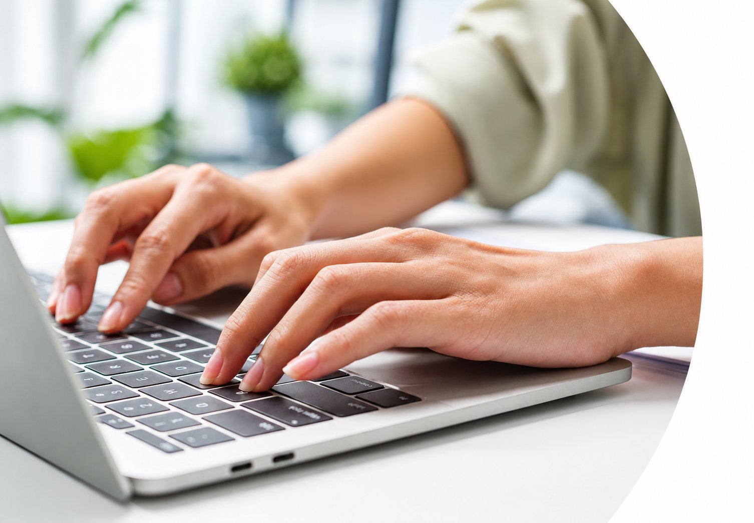 Gros plan sur deux mains en train de taper sur le clavier d’un ordinateur portable argenté posé sur un bureau clair.